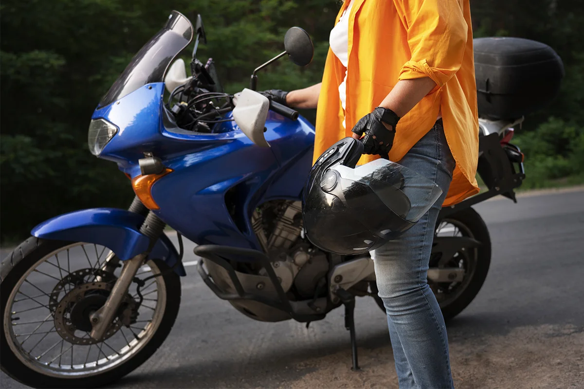 Motocycliste tenant un casque à côté de sa moto bleue, prêt à partir.