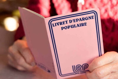 Main tenant un livret d'épargne populaire avec le titre visible.